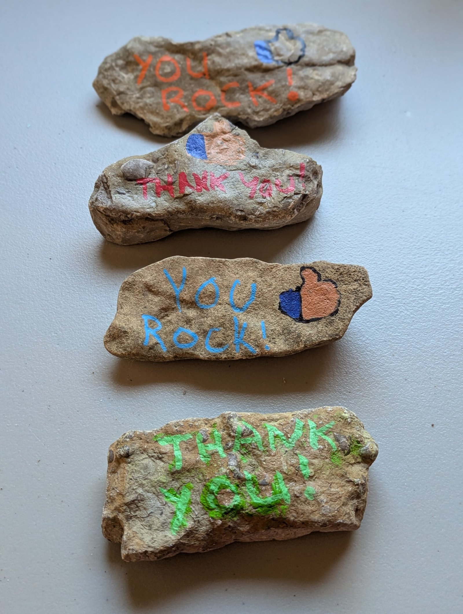Four Kindness Rocks saying You Rock! and Thank You! with thumbs-up symbols