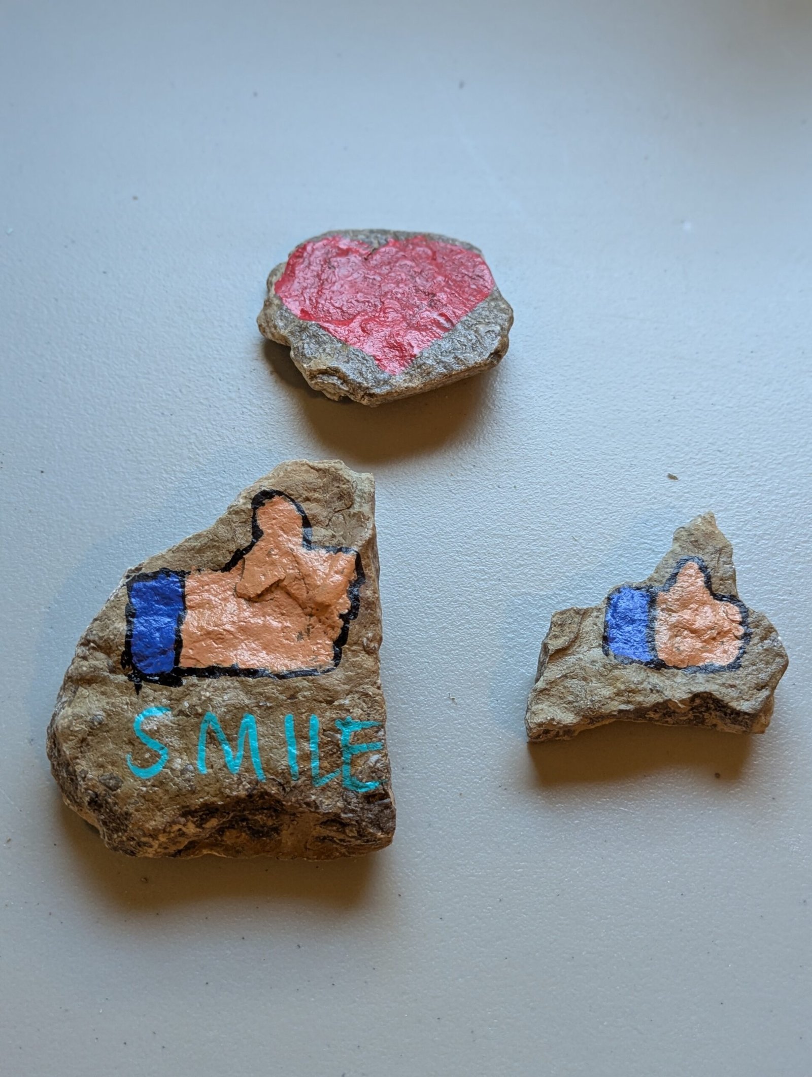 Three Kindness Rocks: red heart, large thumbs-up with Smile, and small thumbs-up